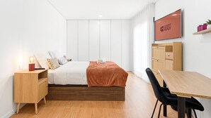 A modern hotel room with a bed, bedside table, TV, and a desk with a chair. - GuestReady-Sunny Modern Retreat in Mira (Mira)