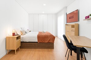 Ein modernes Hotelzimmer mit Bett, Nachttisch, Fernseher und Schreibtisch mit Stuhl.