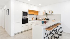 A modern kitchen with white cabinetry, a built-in oven, a microwave, and a bar area with stools. - GuestReady-Sunny Modern Retreat in Mira (Mira)