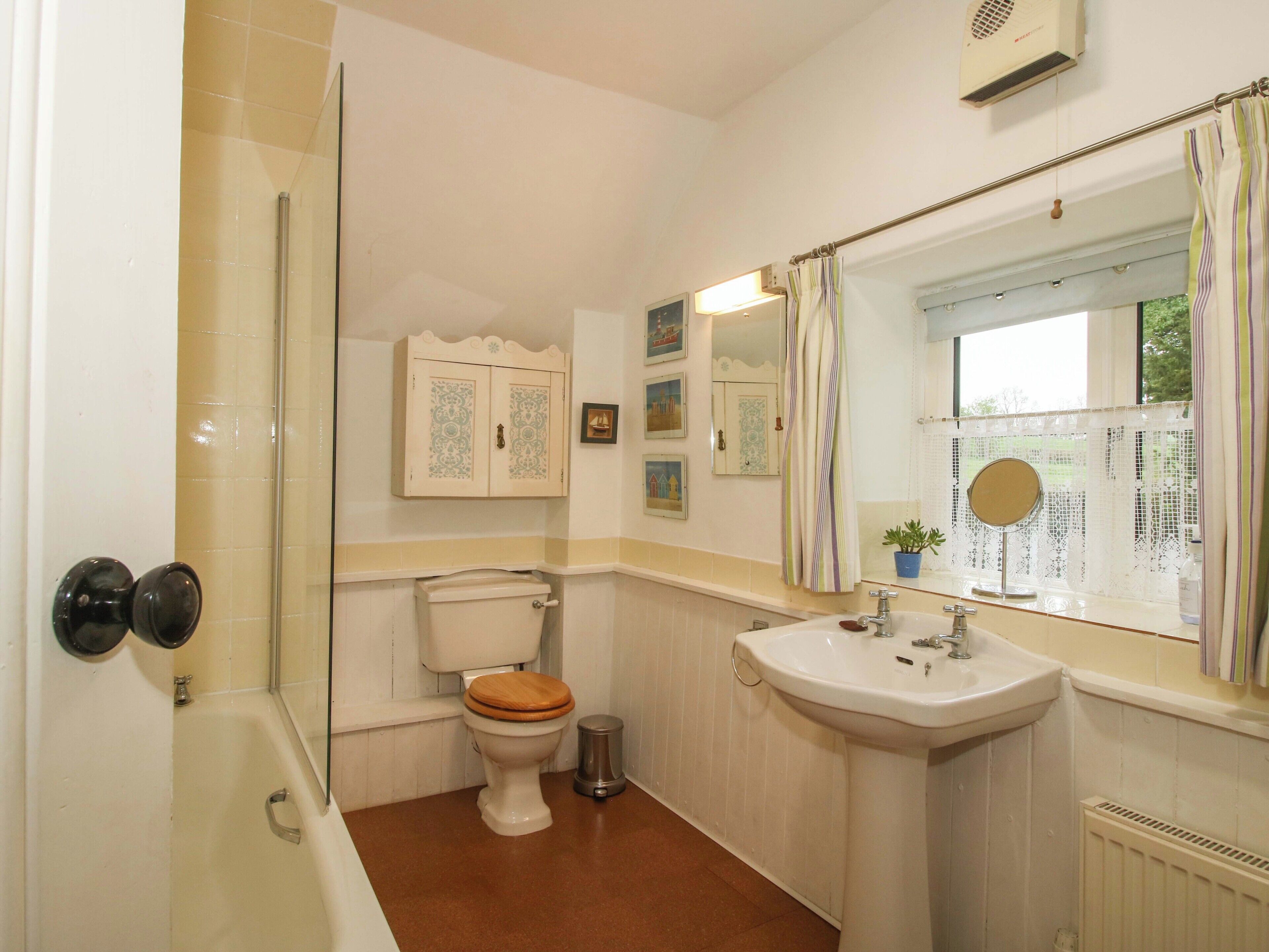 A bathroom with a toilet, sink, shower, and a window with a view.