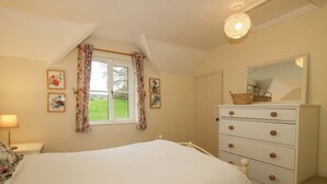 A bedroom with a bed, a dresser, a mirror, and a window with curtains. - Ivy Cottage (Church Stretton)