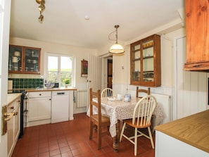 A kitchen with a dining table, chairs, cabinets, and a window. - Ivy Cottage (Church Stretton)