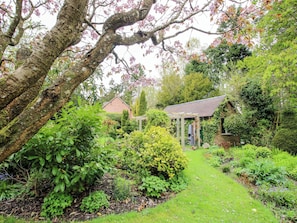 A garden with a pathway leading to a gazebo, surrounded by various plants and trees. - Ivy Cottage (Church Stretton)