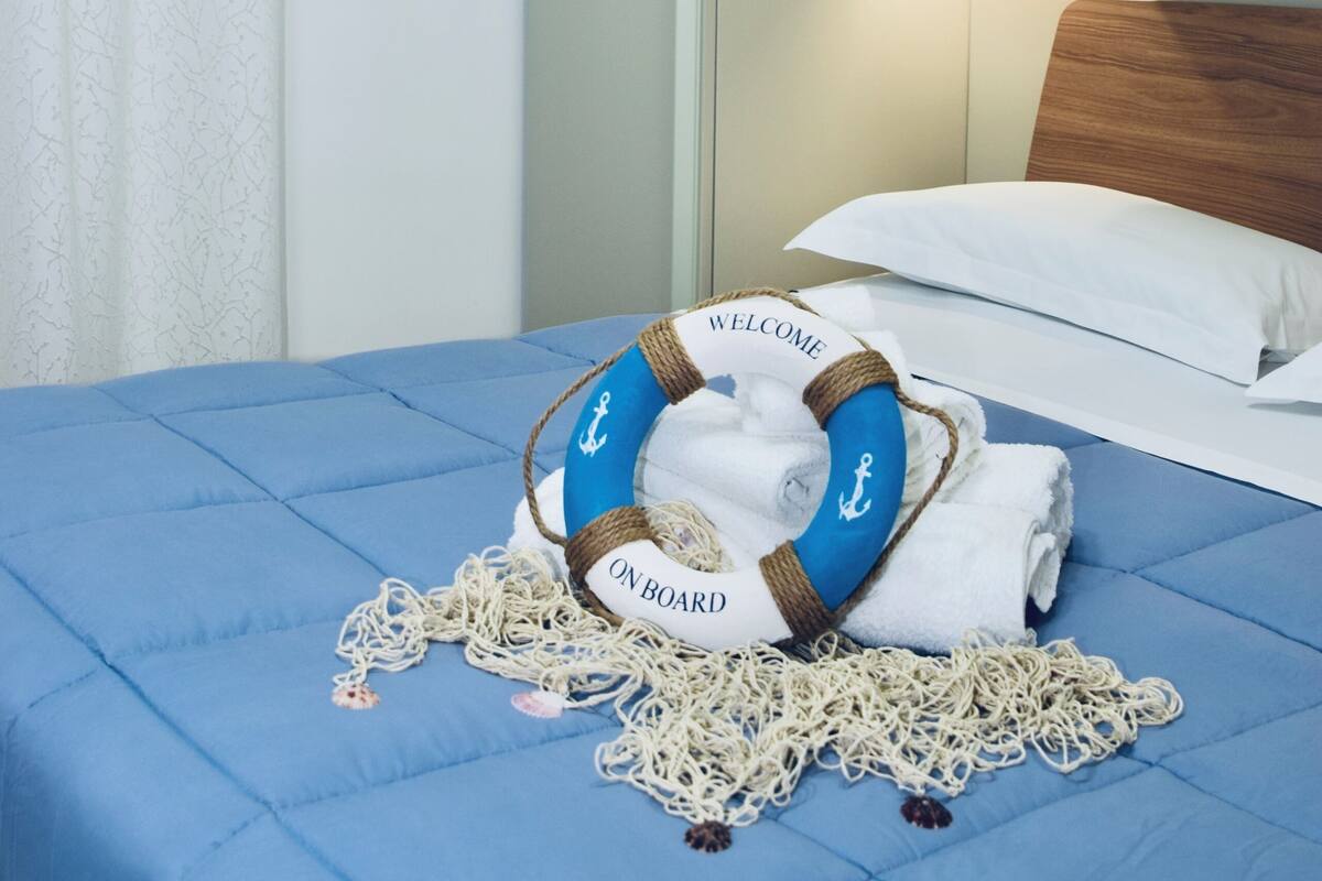 Un dormitorio con una cama, un adorno anclado a la pared, una estantería con un pequeño velero y un círculo salvavidas con el texto 'WELCOME ON BOARD'.