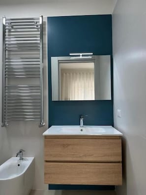 Un baño con tocador moderno, toallero, espejo y bidé.