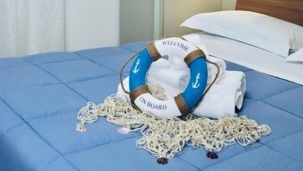 A bed with a blue bedspread, a life jacket, and a welcome mat on it. - B&B le Pontine (Gaeta)