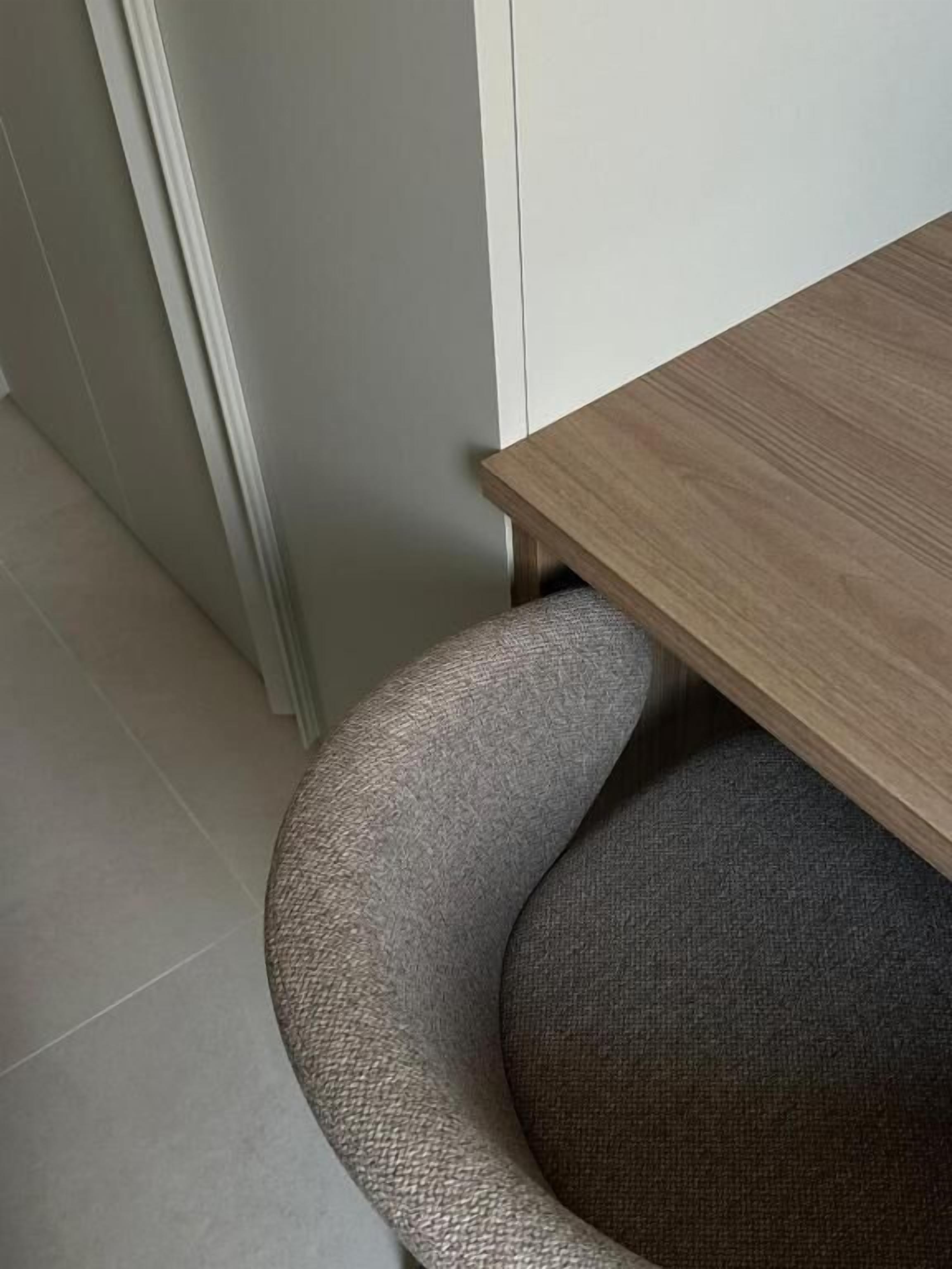 Una esquina de una habitación con una mesa de madera y una silla tapizada de color gris.