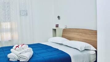 A neatly made bed with a blue quilt, white pillows, and folded towels on a white headboard.