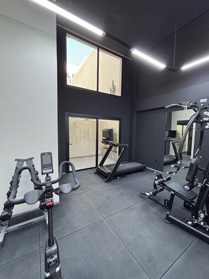 Ein Fitnessstudio mit Trainingsgeräten, großen Fenstern und einem Spiegel.
