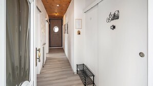 A hallway with a wooden ceiling, a bench, a door with a mirror, and a wall with a 'Bathroom' sign.