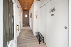 A hallway with a wooden ceiling, a bench, a door with a mirror, and a wall with a 'Bathroom' sign.