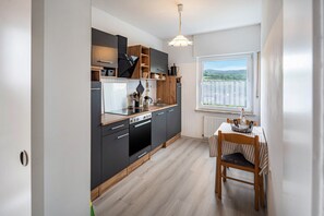 Une cuisine moderne avec des meubles de couleur sombre, un plan de travail en bois et un coin repas comprenant une table et des chaises.
