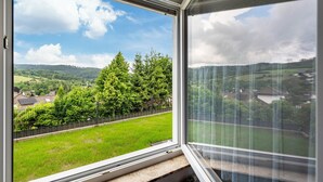 A room with a large window offering a view of a green landscape, a fence, and trees.