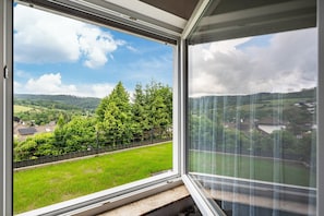 A room with a large window offering a view of a green landscape, a fence, and trees.