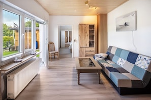 A modern living room with a sofa, a coffee table, and a view through large windows.