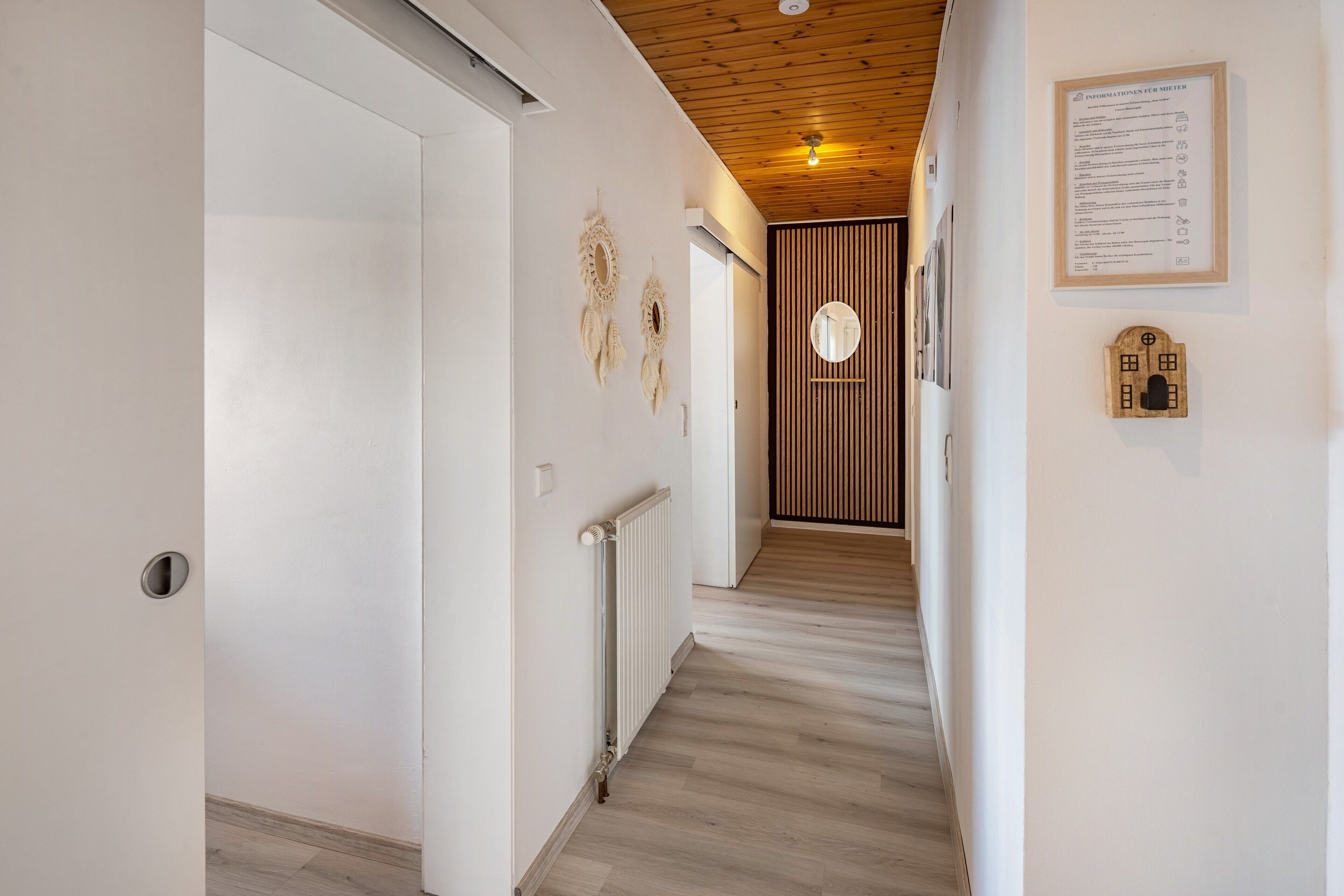A hallway with a wooden ceiling, a white door, a radiator, and a framed informational sign on the wall.