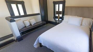 A bedroom with a bed, a bench with pillows, a nightstand with a lamp, and a mirror.