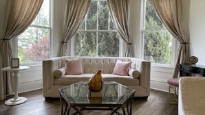 A room with a beige sofa, a glass coffee table, and a view of trees through large windows. - Inn at Park Winters (Winters)