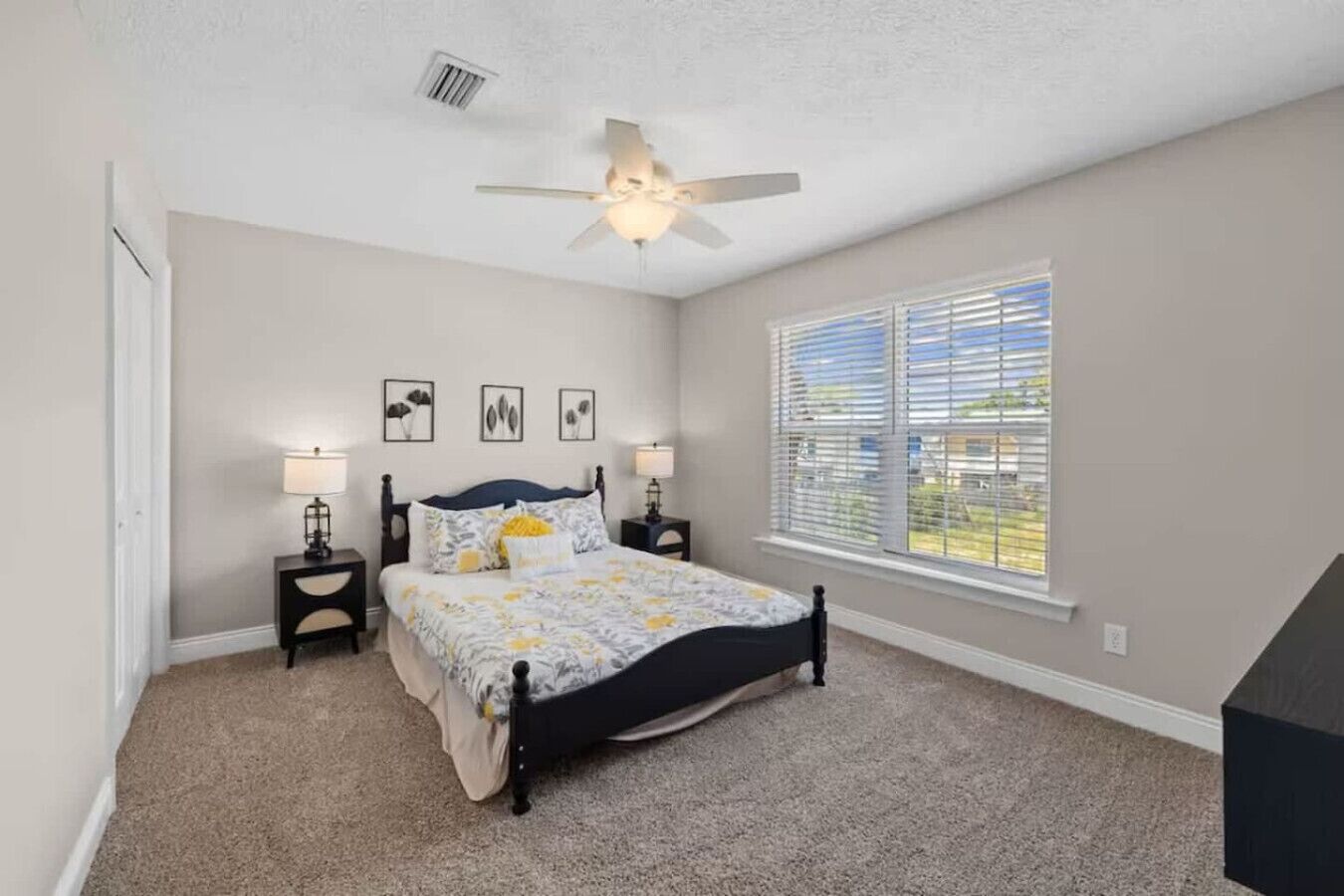 A bedroom with a bed, two bedside tables, a ceiling fan, a window with blinds, and a door.