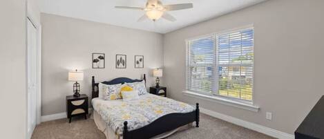 A bedroom with a bed, two bedside tables, a ceiling fan, a window with blinds, and a door.