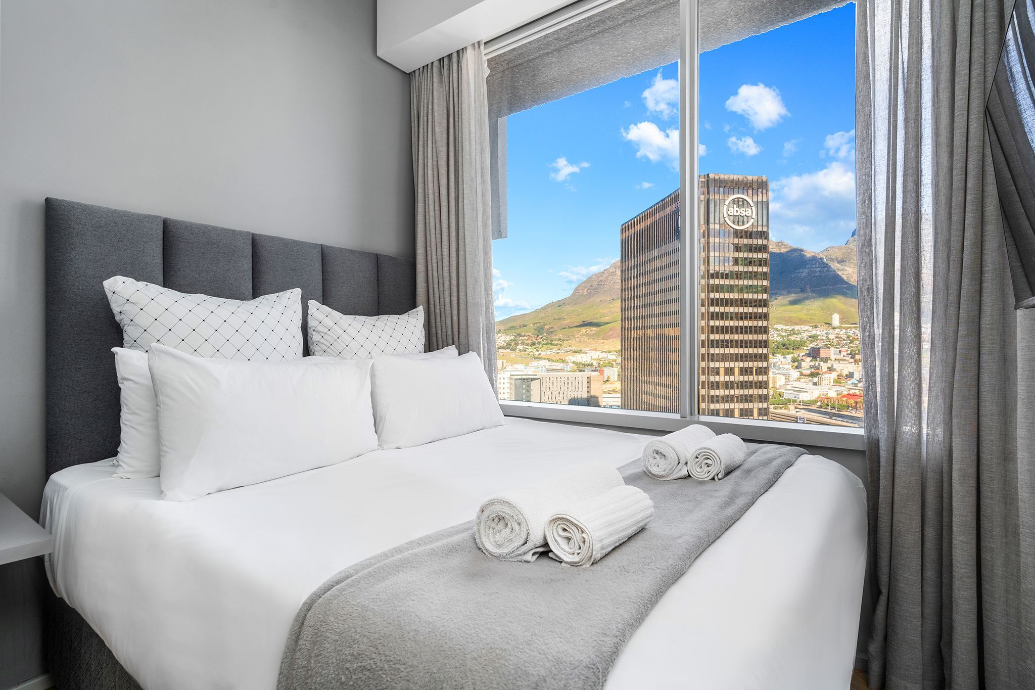 A hotel room with a large bed, a view of a cityscape, and a building with a logo.