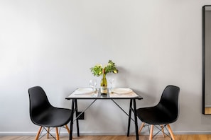 A dining table with two black chairs, a wine bottle, and a vase with flowers. - One Thibault 1927 (Cape Town)