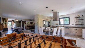 Una cocina moderna con armarios de madera, un comedor con mesa y sillas, y una mesa de fútbol.