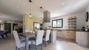 Una cocina moderna con una isla central, iluminación colgante y un comedor con sillas y una mesa.
