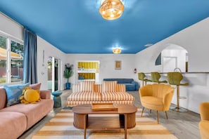 Uma sala de estar moderna com teto azul, um sofá listrado, uma mesa de centro redonda e uma poltrona amarela.