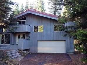 Une maison en bois à deux étages, avec un toit rouge, un garage et un petit porche.