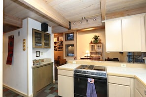 Een keuken met houten kastjes, een fornuis en een eethoek met een tafel en stoelen.