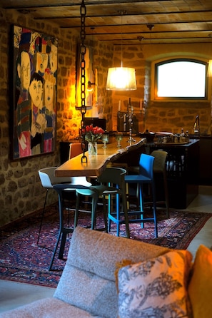 Un comedor con pared de piedra, un cuadro, una lámpara colgante y una zona de bar con taburetes.