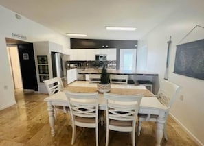 A modern kitchen with white cabinetry, a central island, and a dining area with white chairs. - Sarasota Home With Pool (Osprey)