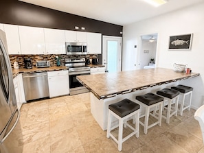 A modern kitchen with white cabinets, a large island with bar stools, a microwave, oven, and a dishwasher.