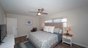 A bedroom with a bed, a ceiling fan, bedside lamps, a nightstand, a TV, and a window. - Sarasota House With Pool (Southgate)