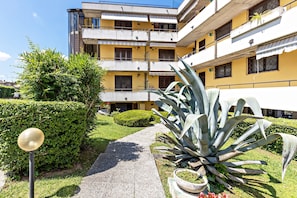 Un immeuble résidentiel à plusieurs étages, doté de balcons, d’un chemin et d’un grand agave.