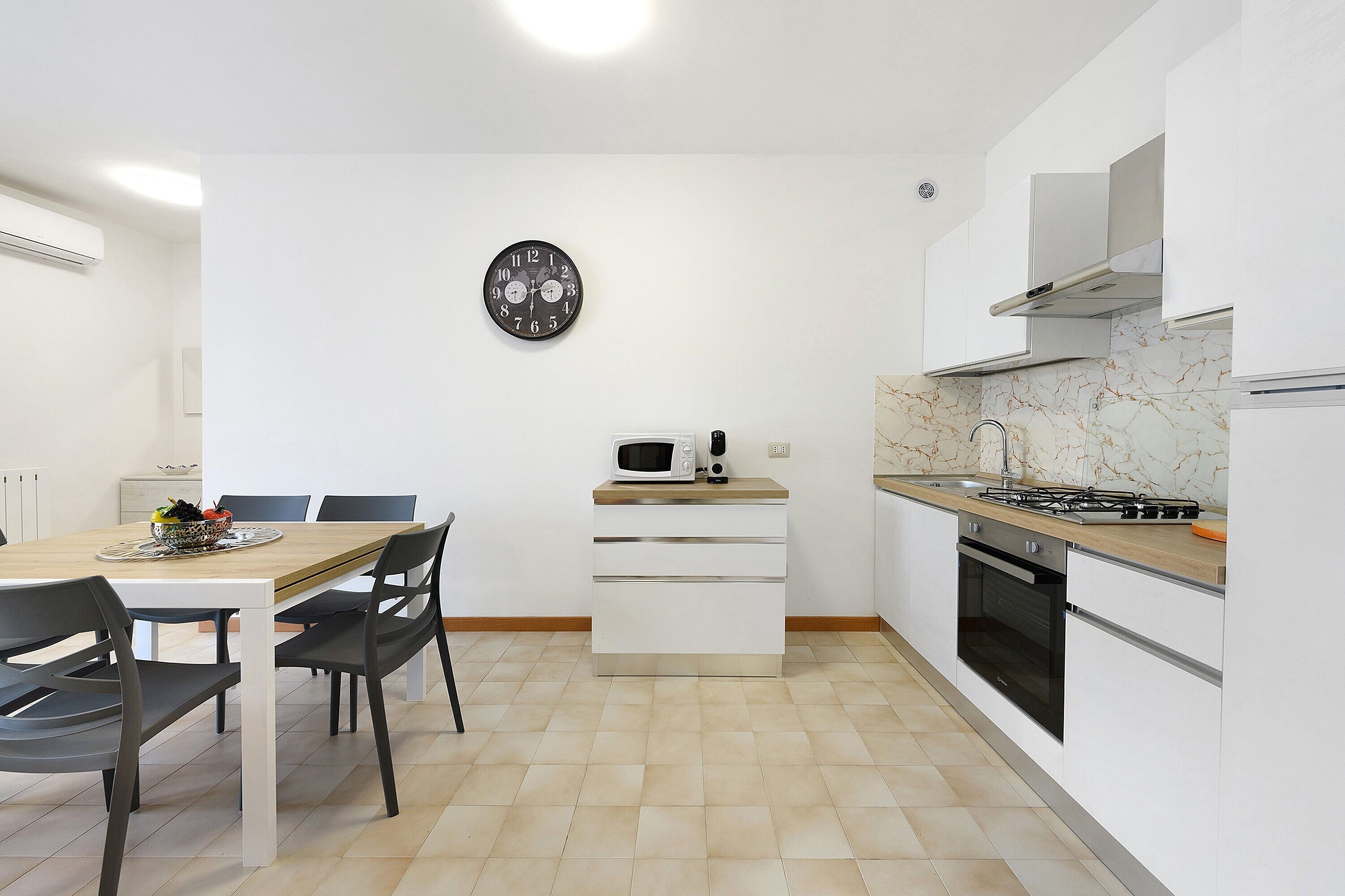 Een moderne keuken met een eettafel, stoelen, een magnetron, een fornuis en een klok aan de muur.
