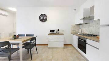 Een moderne keuken met een eettafel, stoelen, een magnetron, een fornuis en een klok aan de muur.
