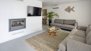Ein modernes Wohnzimmer mit Kamin, Flachbildfernseher, grauem Sofa, Glastisch und einer Wanddekoration.