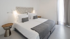 Ein modernes Schlafzimmer mit einem großen Bett, zwei Nachttischen, einem dekorativen Kopfteil und einem Fenster mit transparenten Vorhängen.