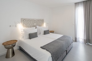 Ein modernes Schlafzimmer mit einem großen Bett, zwei Nachttischen, einem dekorativen Kopfteil und einem Fenster mit transparenten Vorhängen.