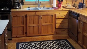 A kitchen with wooden cabinets, a sink, a stove, and a window with a view of the outdoors. - Peaceful 2-bedroom cabin with AC in charming Logan Sleeps 8 (Logan)