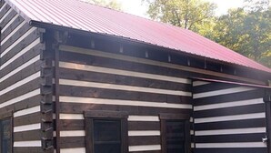 A log cabin with a metal roof, a hot tub, and a fenced yard. - Peaceful 2-bedroom cabin with AC in charming Logan Sleeps 8 (Logan)