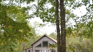 A cabin with a wooden exterior, a balcony, and a grassy area in front. - Peaceful 2-bedroom cabin with AC in charming Logan Sleeps 8 (Logan)