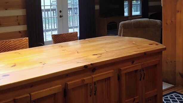 A wooden cabin interior with a large wooden table, two chairs, a television, and a fireplace. - Peaceful 2-bedroom cabin with AC in charming Logan Sleeps 8 (Logan)