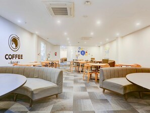 A coffee house with a modern interior, featuring round tables, cushioned seating, and a wall with a coffee cup logo. - Collection O Sector 64 Near Worldmark Gurugram (Gurugram)