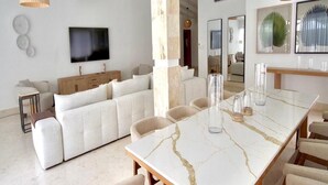 Amplia sala de estar con un sofá seccional blanco grande, una mesa de comedor de mármol y un techo alto con vigas a la vista.
