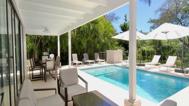 Un espacio al aire libre techado con piscina, sillas de descanso y una mesa.