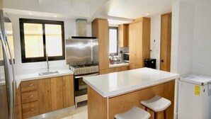 Una cocina moderna con armarios de madera, una estufa de acero inoxidable, una isla grande con taburetes y un refrigerador.