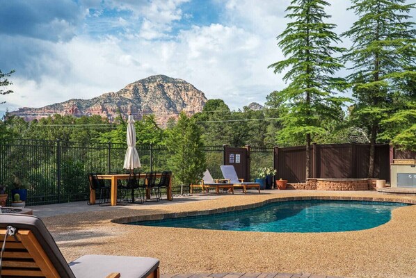 Ein Garten mit Swimmingpool, Liegestühlen, einem Tisch und Blick auf einen Berg.